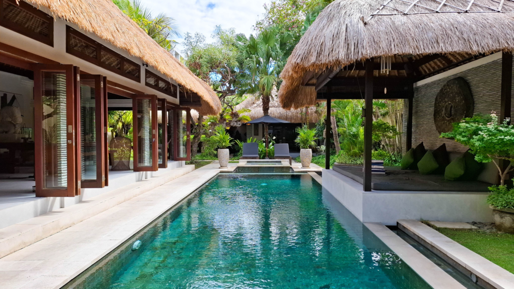 Villa Bugis serene private villa with traditional thatched roofs, a crystal-clear pool lined by tropical greenery, and open-air architecture for a relaxing Balinese retreat.