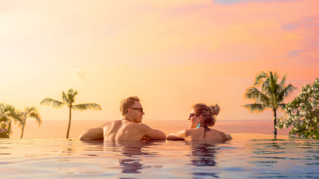 Couple relaxing in an infinity pool during sunset with palm trees in the background, showcasing the tranquil atmosphere of the best area to stay in Bali in 2025.