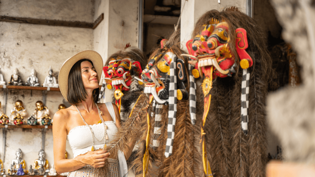 Tourist shopping in Bali Seminyak, admiring traditional Balinese Barong masks at a local artisan market.