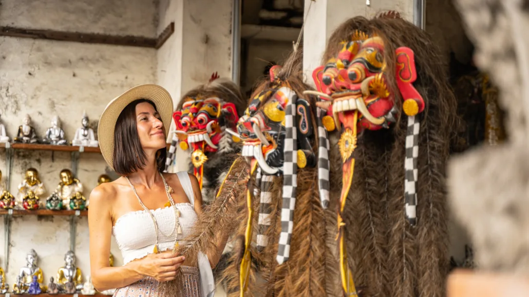 Tourist shopping in Bali Seminyak, admiring traditional Balinese Barong masks at a local artisan market.
