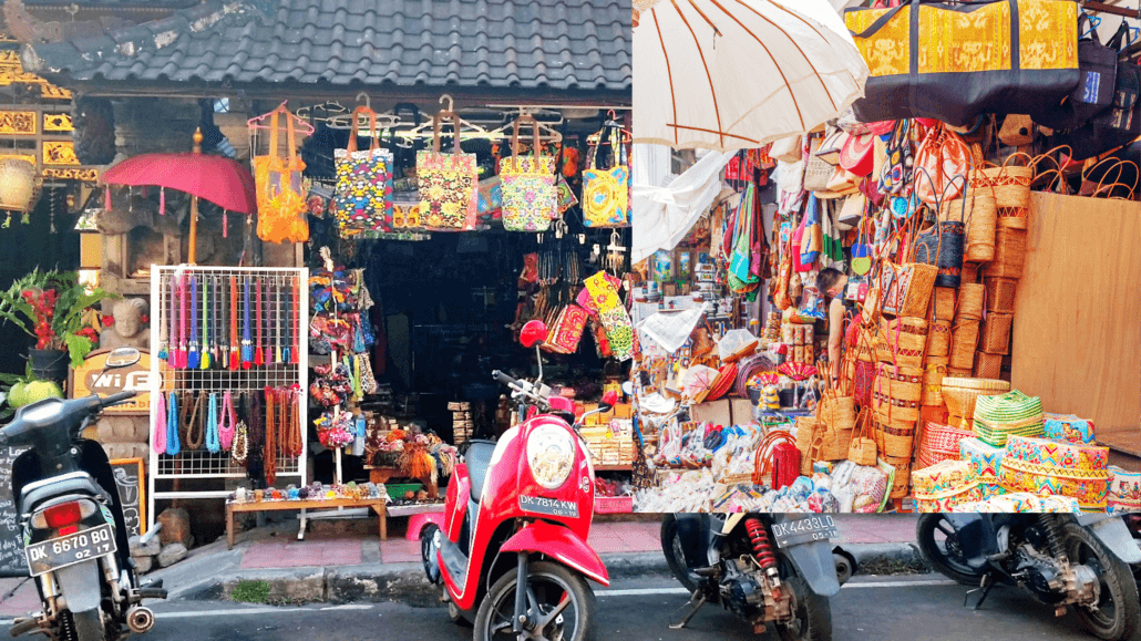 Traditional Balinese market in Seminyak, Bali, displaying colorful handmade bags, woven baskets, and souvenirs, with scooters parked outside.