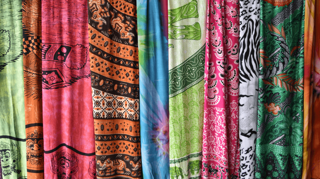 Vibrant traditional Balinese sarongs with intricate patterns and cultural designs displayed at a market in Seminyak, Bali.