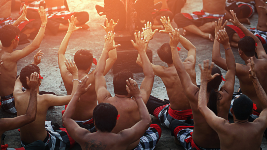 Traditional Kecak dance performance at sunset in Bali, with performers raising their hands in unison during a cultural show.