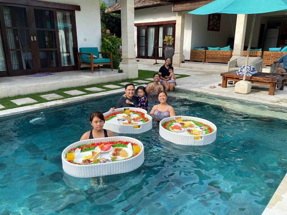 Guests enjoying floating breakfast in a private pool at Villa Darma by Villa Bugis Seminyak, Bali.