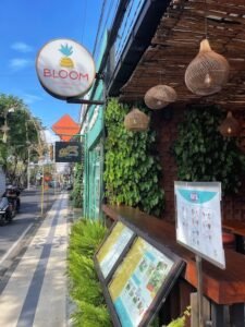 Entrance of Bloom Cafe in Seminyak with tropical greenery and stylish decor on a vibrant street.