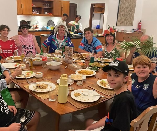 A multi-generational family enjoying a fun, catered dinner gathering at a large table while a private chef cooks in the background at Villa Alore.