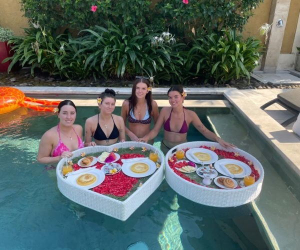Four young women in swimwear enjoying two heart-shaped floating breakfast trays in the private swimming pool at Villa Gembira.