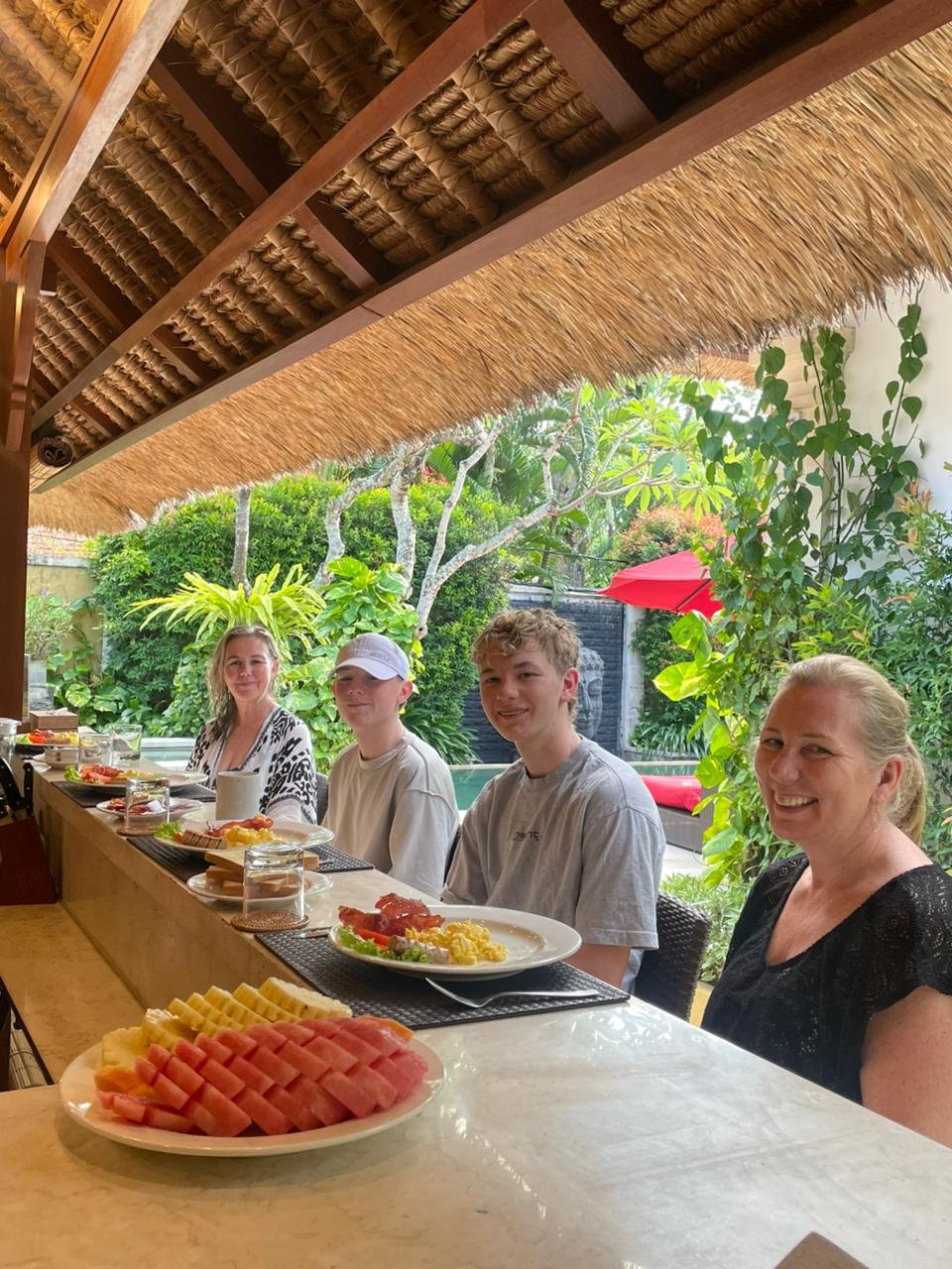 A family of four smiling while enjoying a fresh morning breakfast at the outdoor bar counter overlooking the tropical garden at Villa Jaclan in Seminyak.