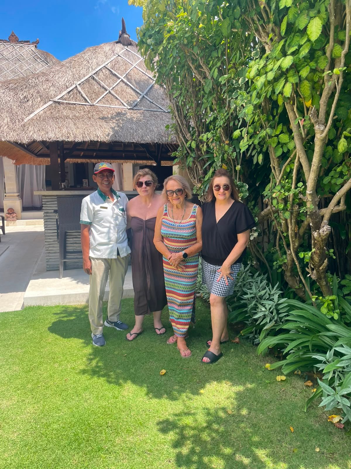 Three female guests smiling and posing for a photo with a friendly villa staff member in the lush tropical garden at Villa Rama in Seminyak.