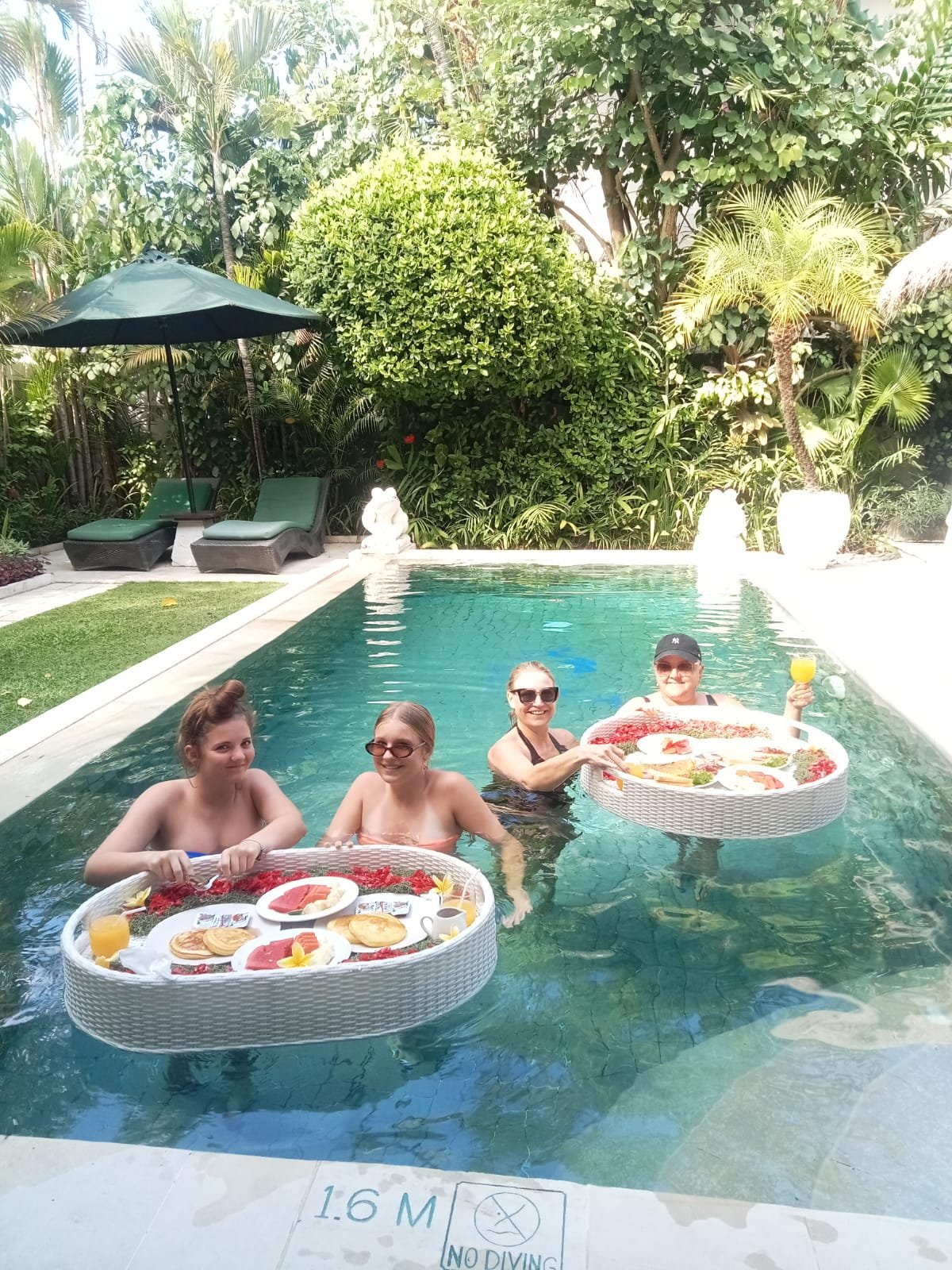 Three female guests relaxing in the private swimming pool while enjoying a delicious floating breakfast experience on woven trays at Villa Krisna.