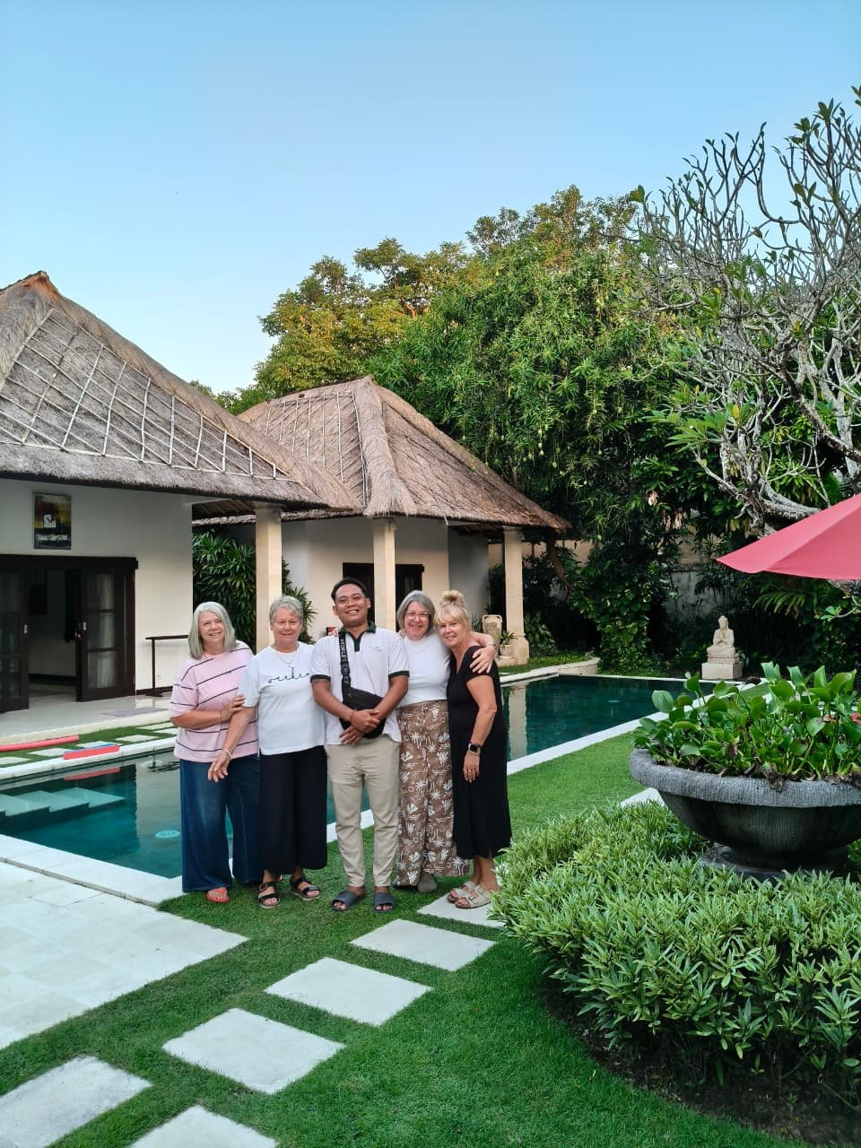 Four female guests posing for a group photo with a friendly villa staff member in the lush garden next to the swimming pool at Villa Kebun.
