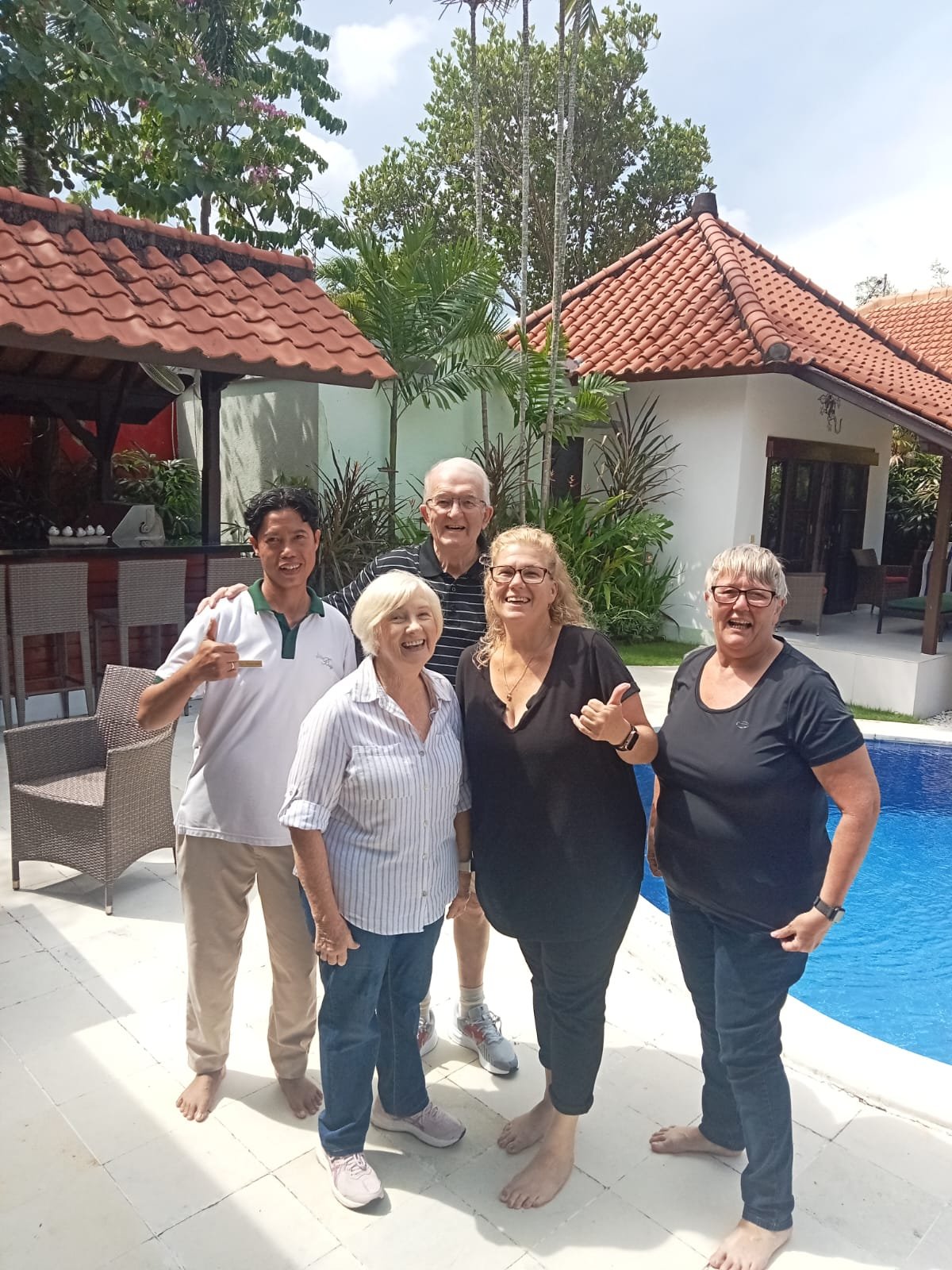 Four happy senior guests posing for a group photo with a smiling villa staff member next to the private swimming pool at Villa Ginger.