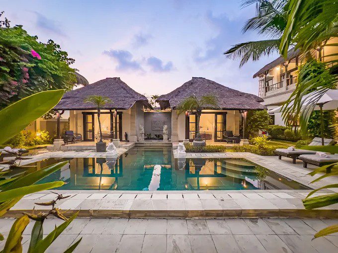 The main outdoor relaxation deck at Villa Arjuna Seminyak by Villa Bugis Seminyak villas in the evening, with the pool surrounded by exotic greenery.