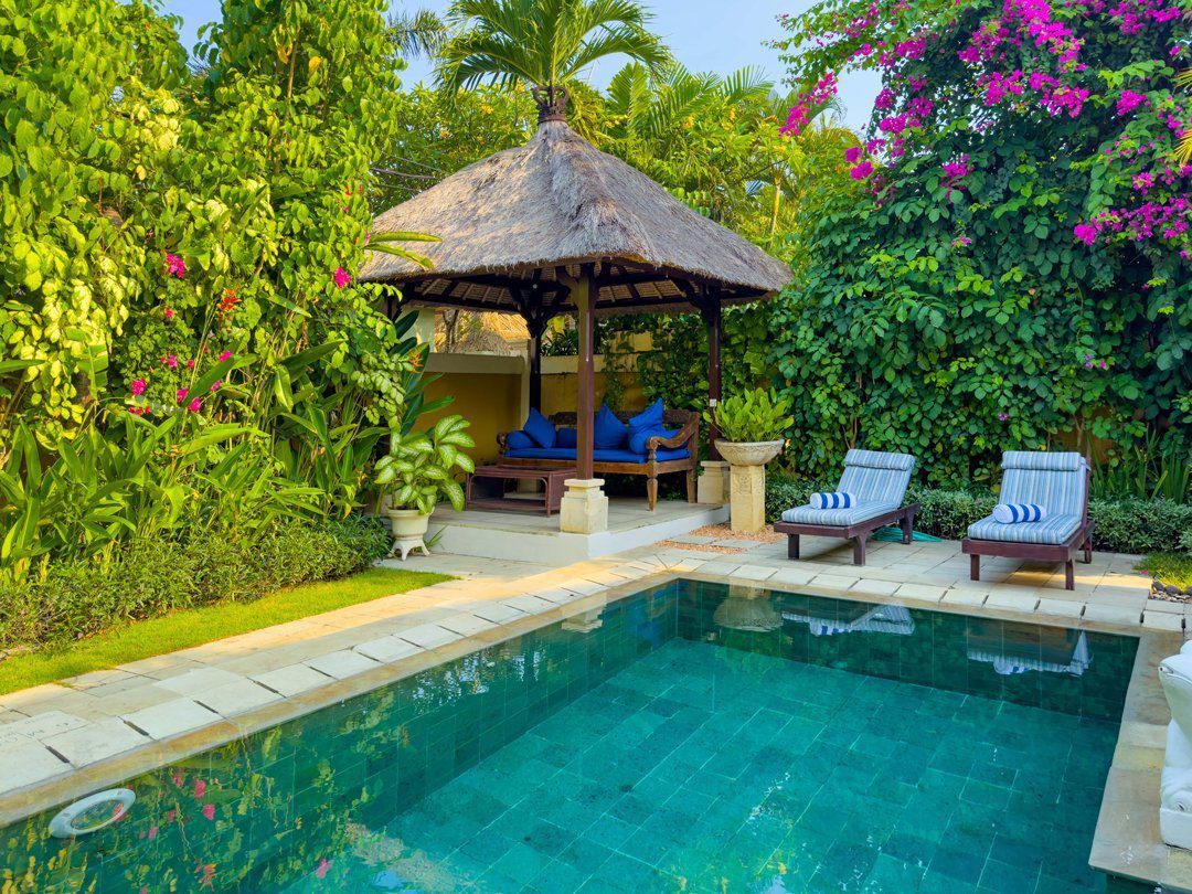 Pristine private outdoor swimming pool at Villa Arjuna Seminyak by Villa Bugis, a luxury villa Seminyak featuring comfortable sun loungers and a lush tropical garden.