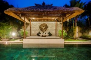 Thatched poolside bale with daybed and cushions lit at night at Villa Damai Seminyak