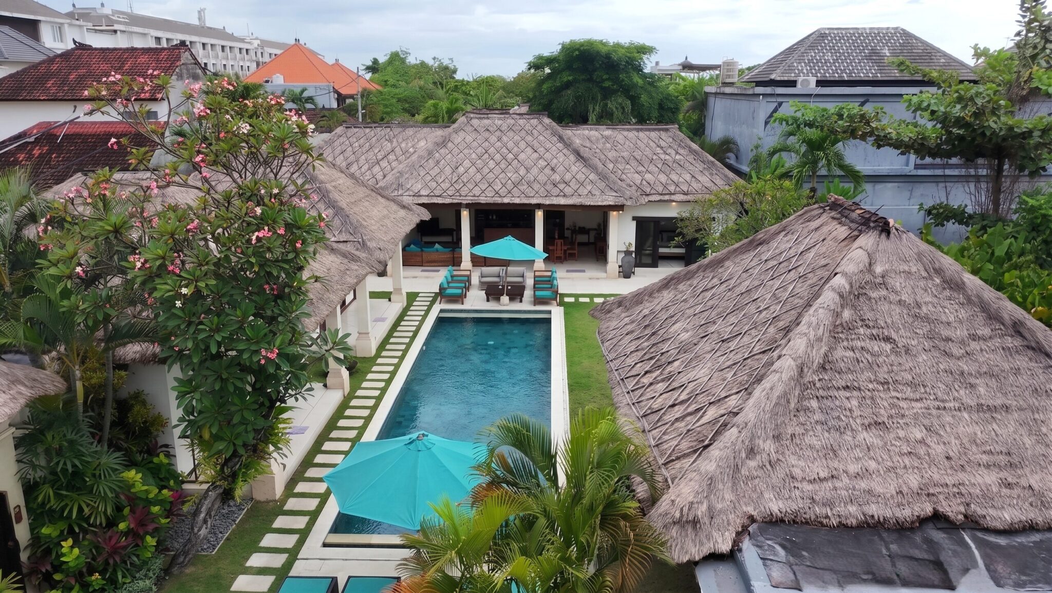 Aerial view of the large private pool at Villa Darma Seminyak by Villa Bugis, framed by traditional thatched roofs in this villa Seminyak.