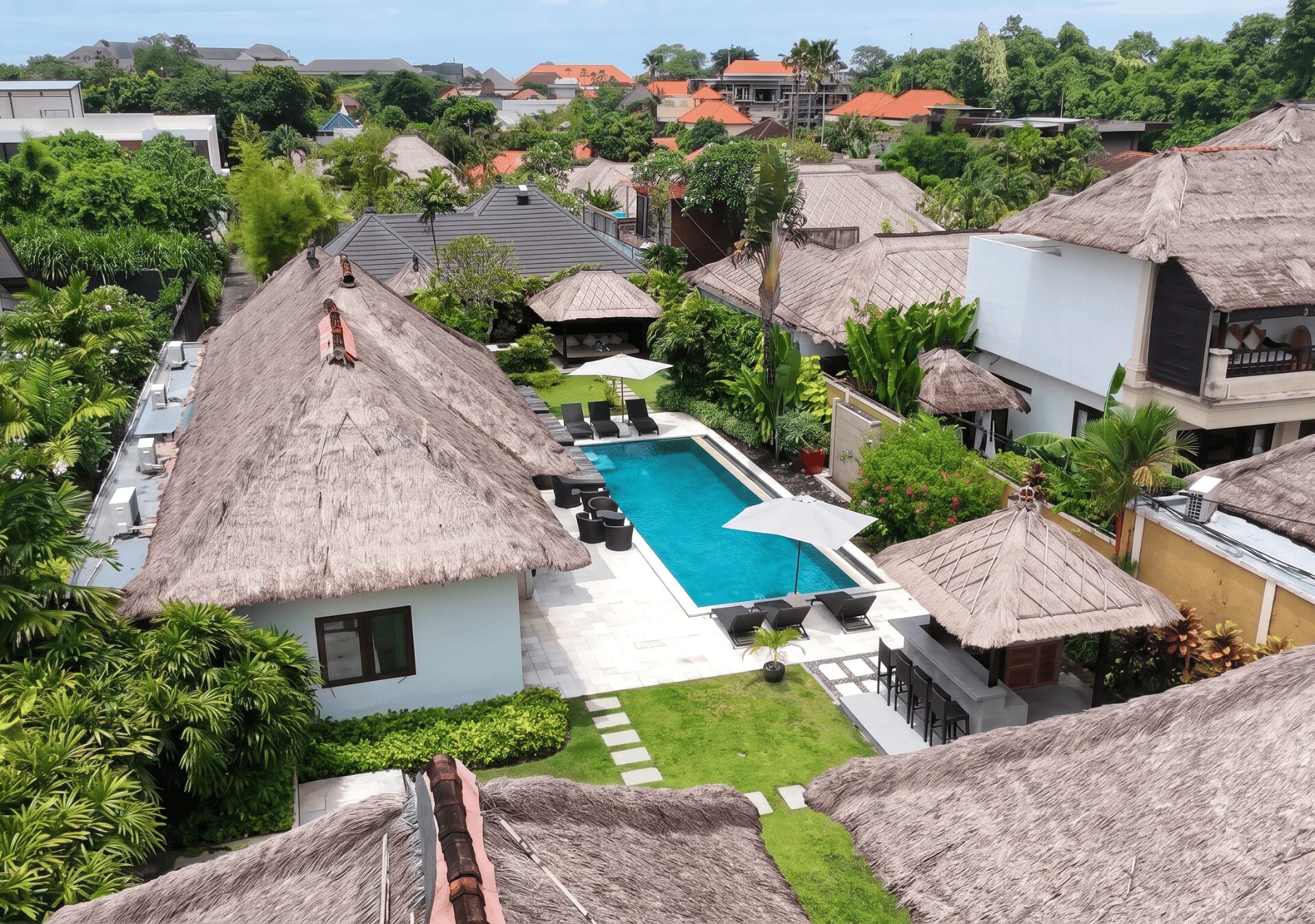 Bird's-eye aerial view highlighting the sprawling pool deck, traditional thatched roof pavilion, and lush greenery at Villa Gembira Seminyak by Villa Bugis Seminyak villas.
