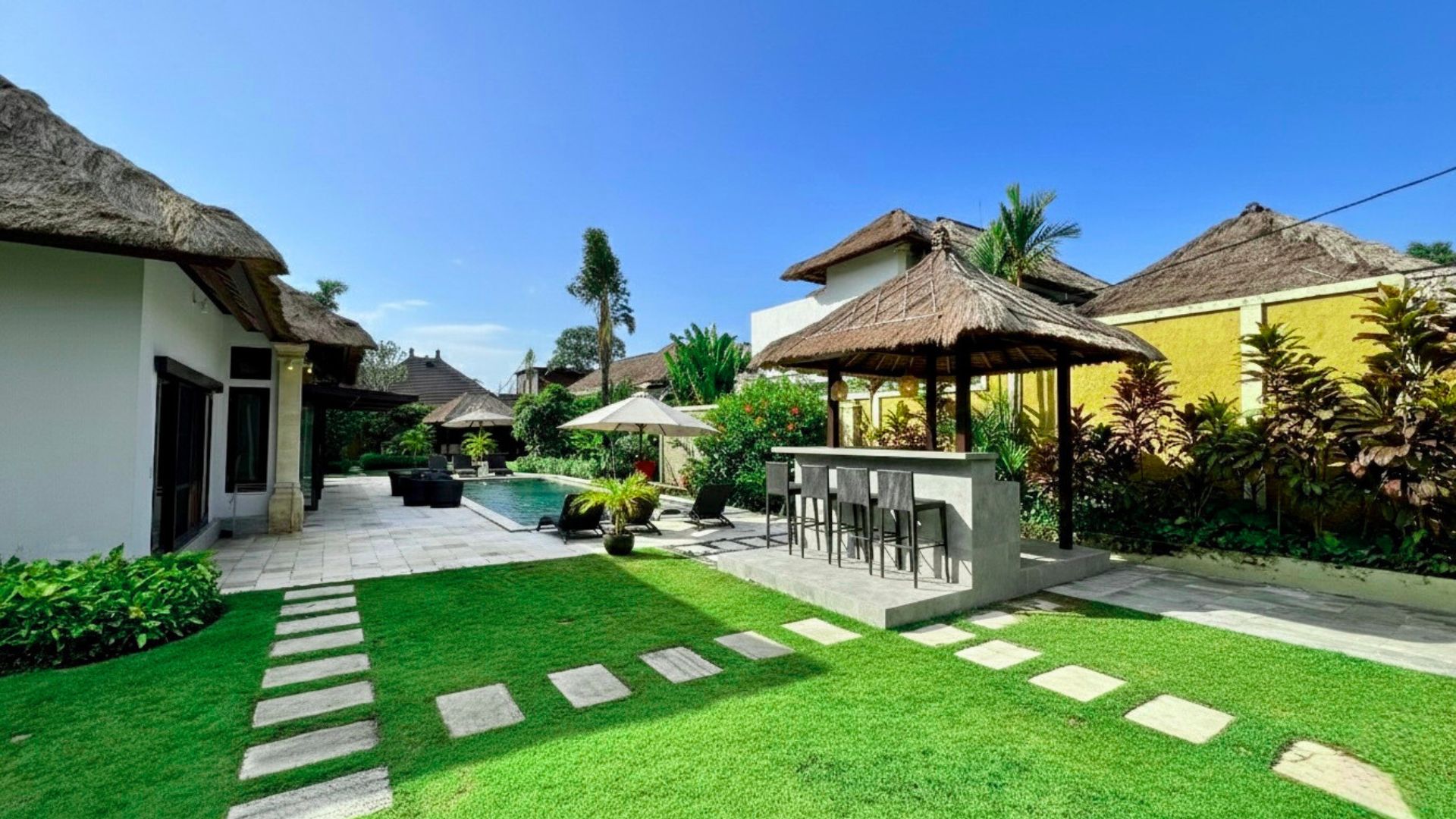 Manicured green lawn and tropical landscaping enclosing the pool deck at Villa Gembira Seminyak by Villa Bugis villa Seminyak.