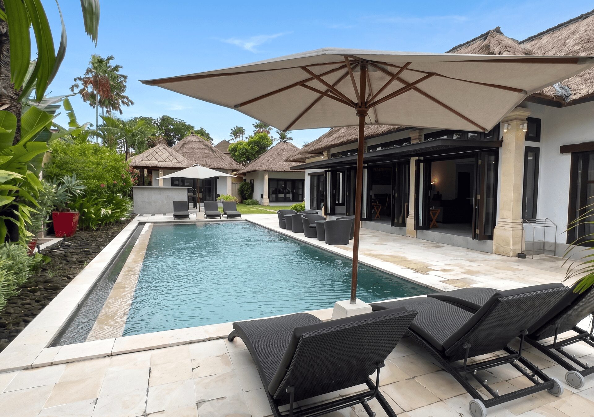Sunny daytime view of the spacious poolside garden area at Villa Gembira Seminyak by Villa Bugis Seminyak villas, perfect for family relaxation.