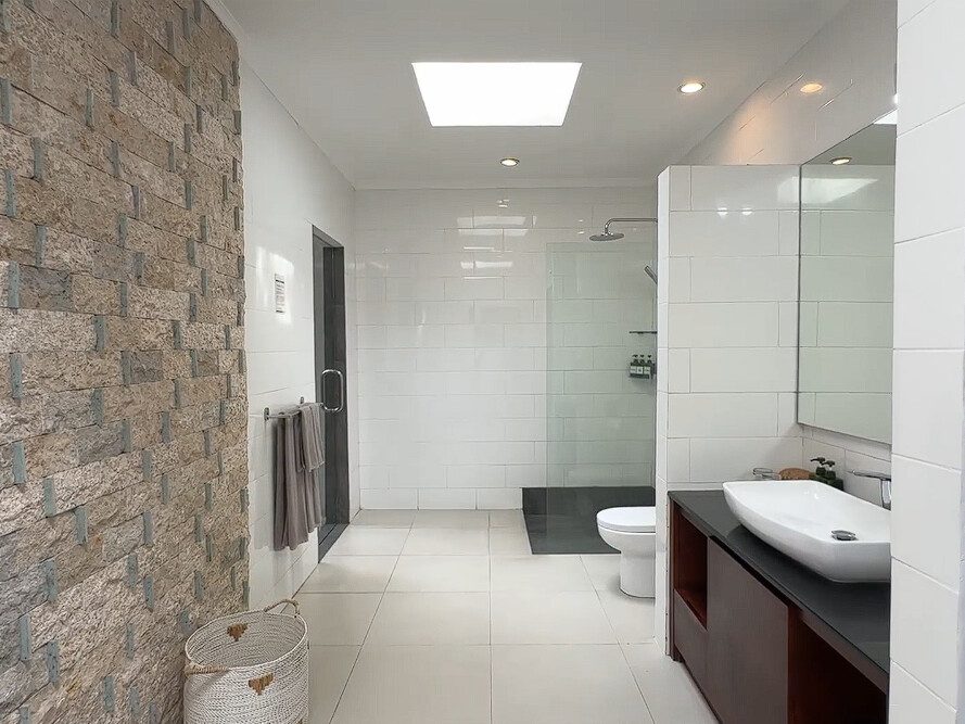 Pristine shower area enclosed by natural stone textures and tropical plants in the bathroom of bedroom 2 at Villa Ginger Seminyak by Villa Bugis Seminyak villas.