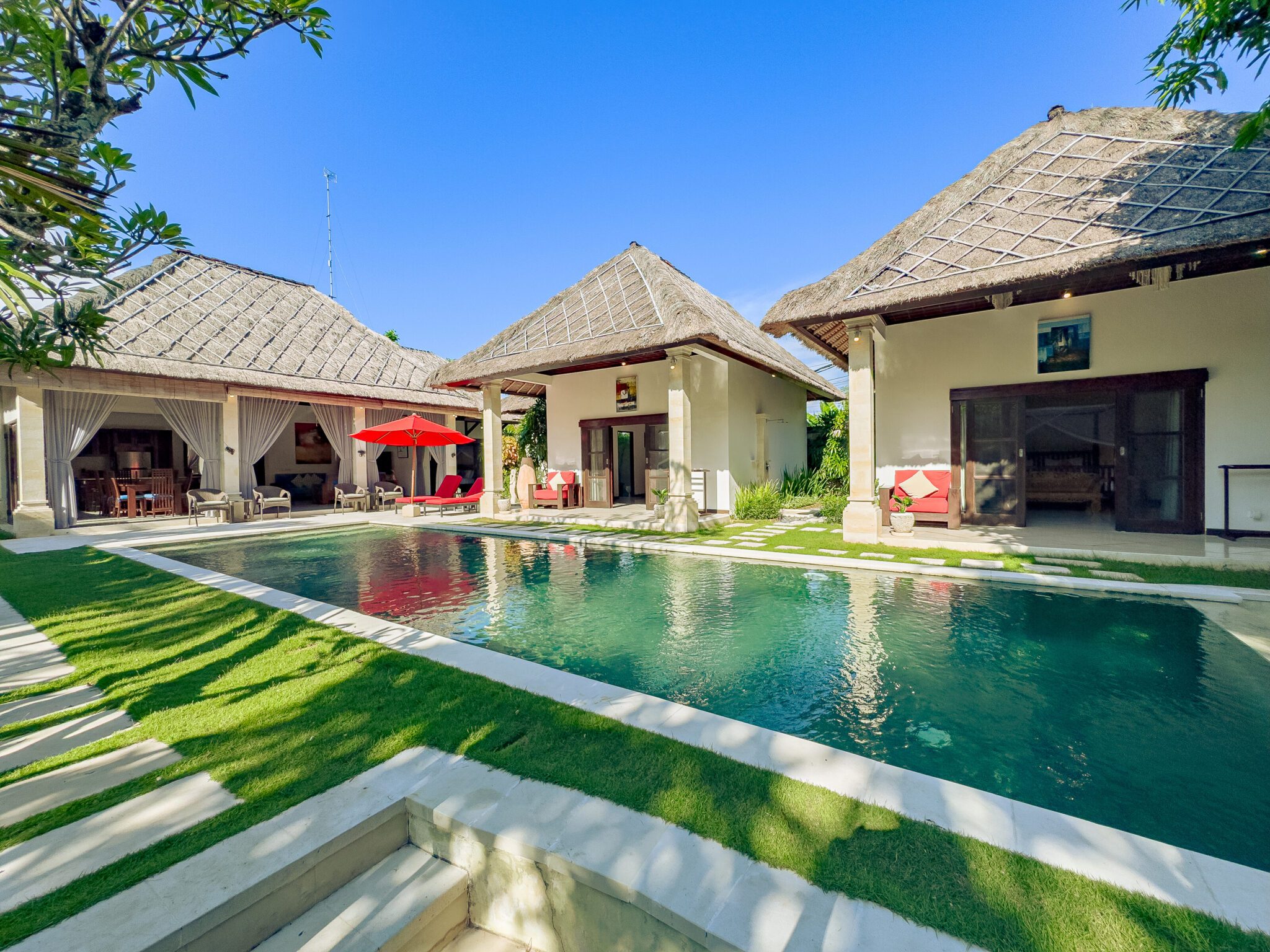 Vibrant tropical garden and poolside relaxation zone under a clear sunny sky at Villa Kebun Seminyak by Villa Bugis, ideal for a villa Seminyak holiday.