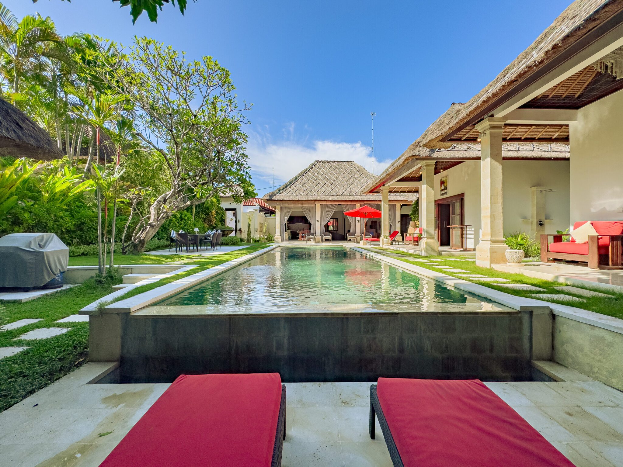 Sparkling pool waters reflecting sunlight beside traditional Balinese garden features at Villa Kebun Seminyak by Villa Bugis Seminyak villas.