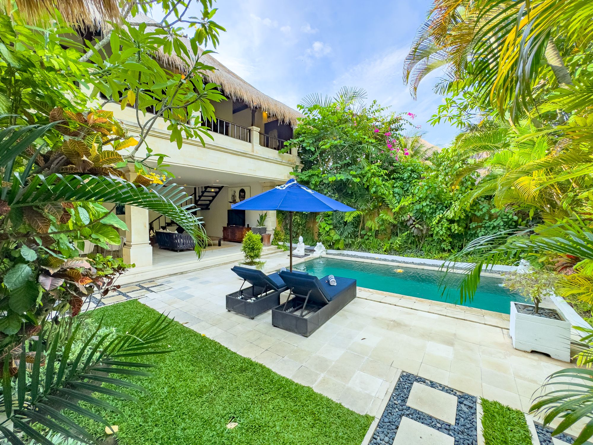 Manicured green lawn and tropical palms surrounding the clear blue pool at Villa Nakula Seminyak by Villa Bugis Seminyak villas.
