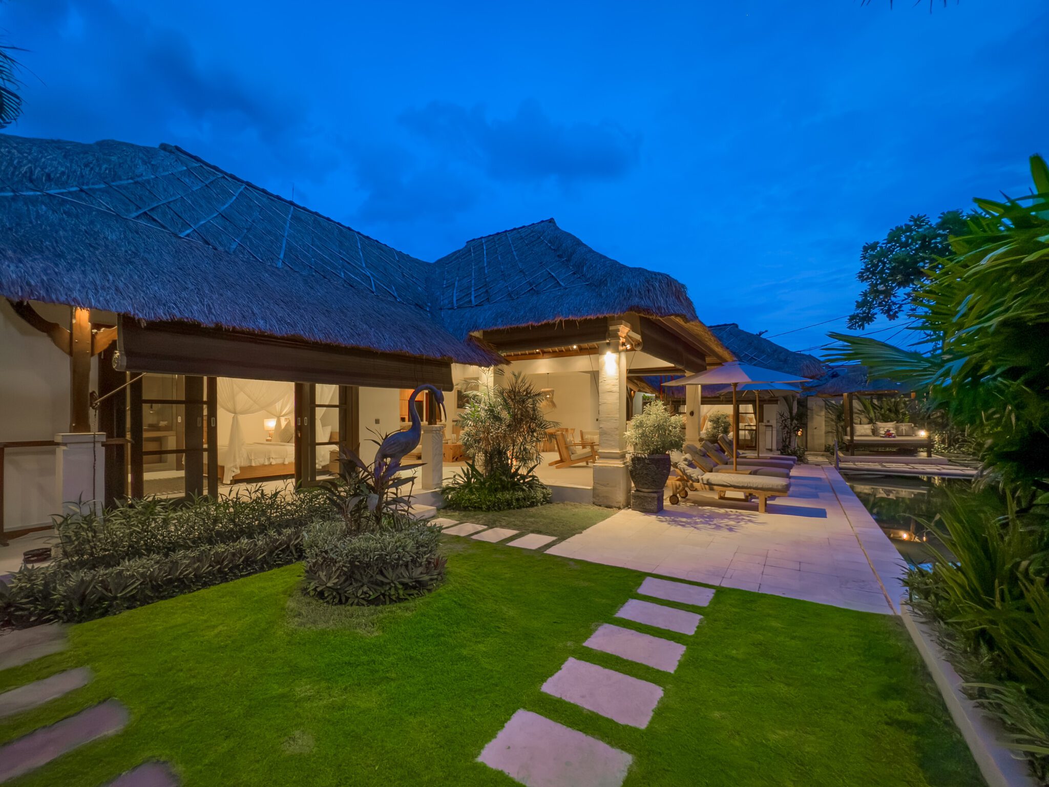Warm night lighting illuminating the poolside terrace and tropical garden at Villa Olive Seminyak by Villa Bugis Seminyak villas.