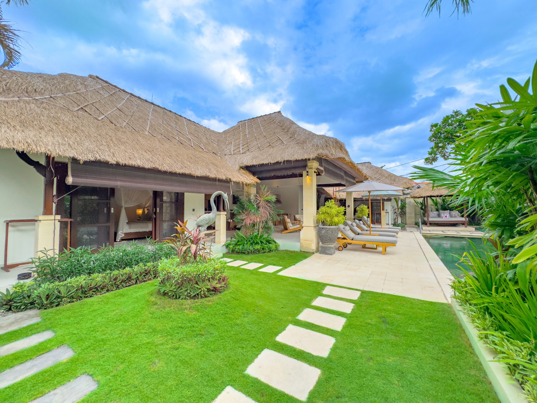 Manicured lawn and green tropical palms surrounding the crystal-clear pool at Villa Olive Seminyak by Villa Bugis Seminyak villas.