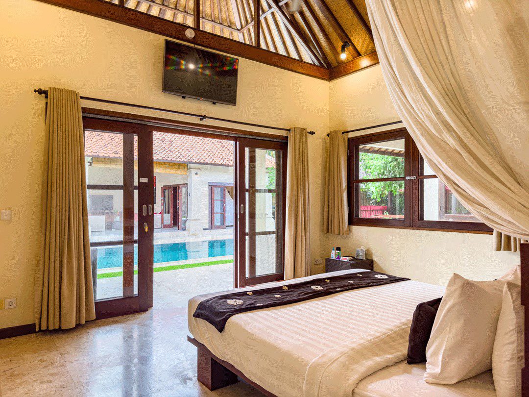 Airy bedroom 2 interior with pool views at Villa Santi Seminyak by Villa Bugis Seminyak villas, equipped with air conditioning and warm lighting.