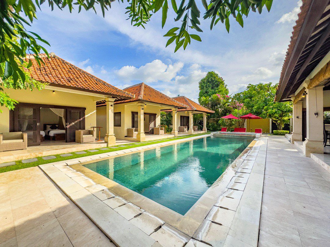 Pristine private outdoor swimming pool surrounded by comfortable sun loungers and a lush tropical garden at Villa Santi Seminyak by Villa Bugis, a luxury villa Seminyak.