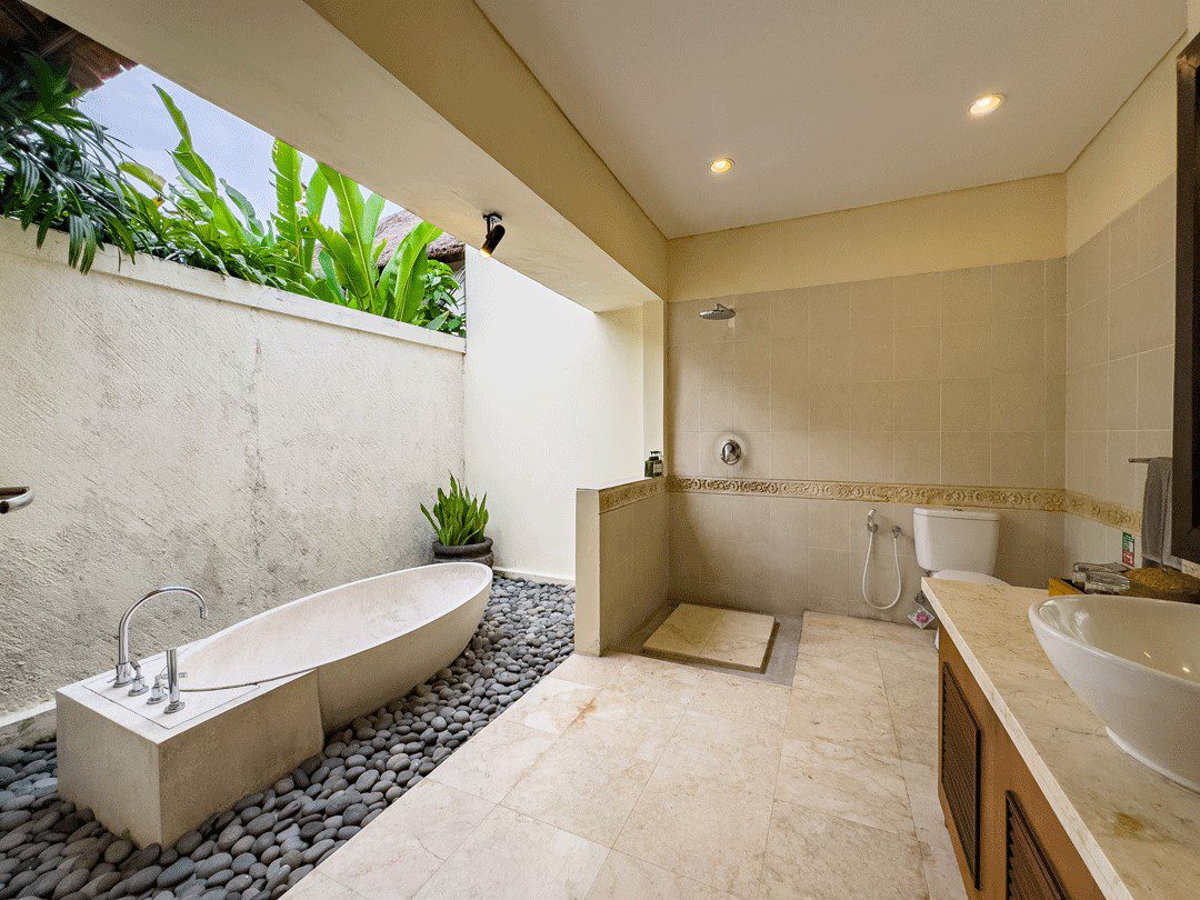 Well-lit vanity mirror, stone textures, and a soaking bathtub in the bathroom of bedroom 3 at Villa Santi Seminyak by Villa Bugis Seminyak villas.