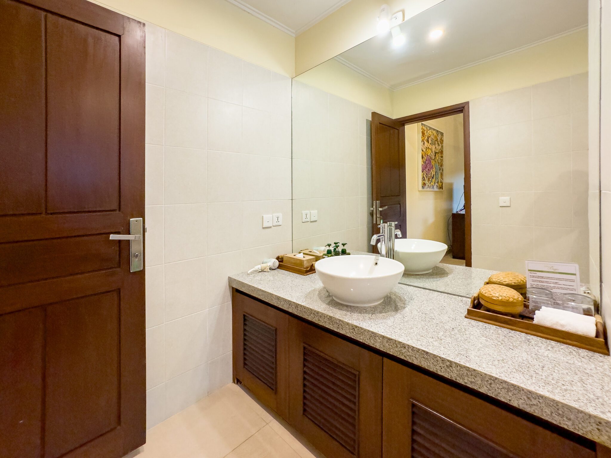Well-lit vanity mirror and stone textures in the bathroom of bedroom 3 at Villa Saphir Seminyak by Villa Bugis Seminyak villas.