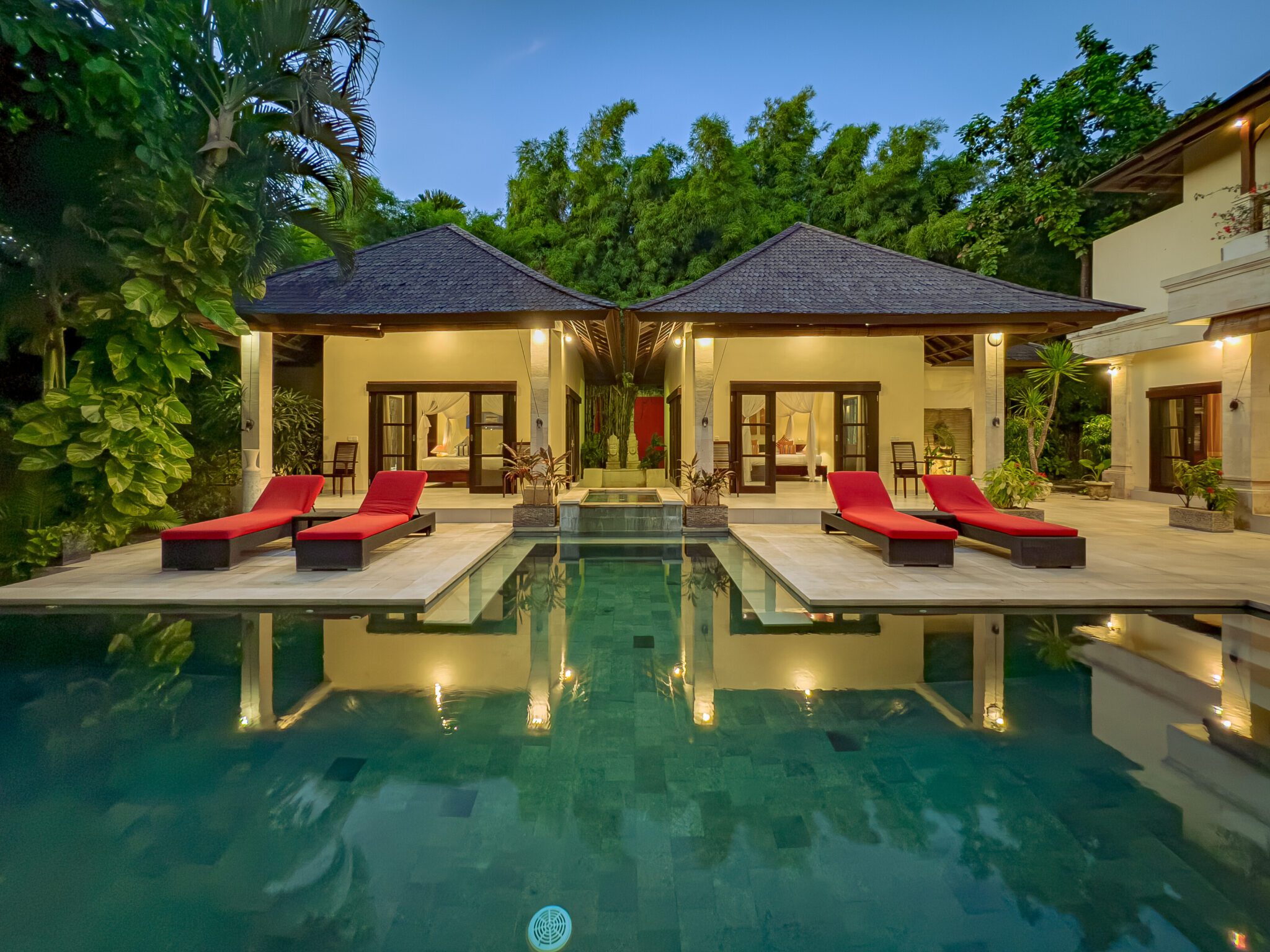 Cozy night view of the illuminated poolside patio and tropical garden at Villa Tresna Seminyak by Villa Bugis villa Seminyak.