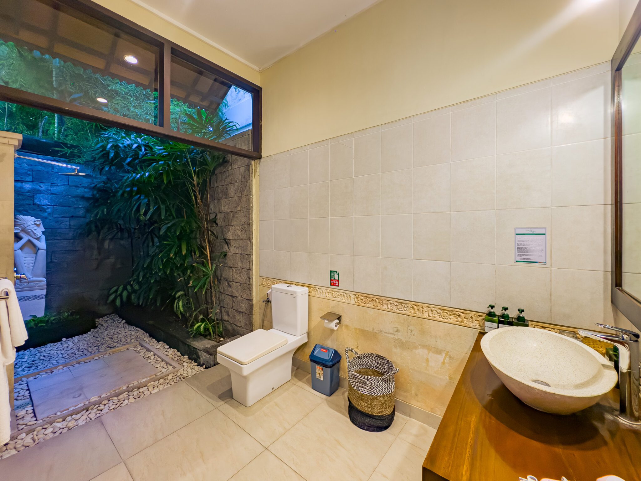 Open-air ensuite shower room with stone accents lit in the evening at Villa Tresna Seminyak by Villa Bugis Seminyak villas.