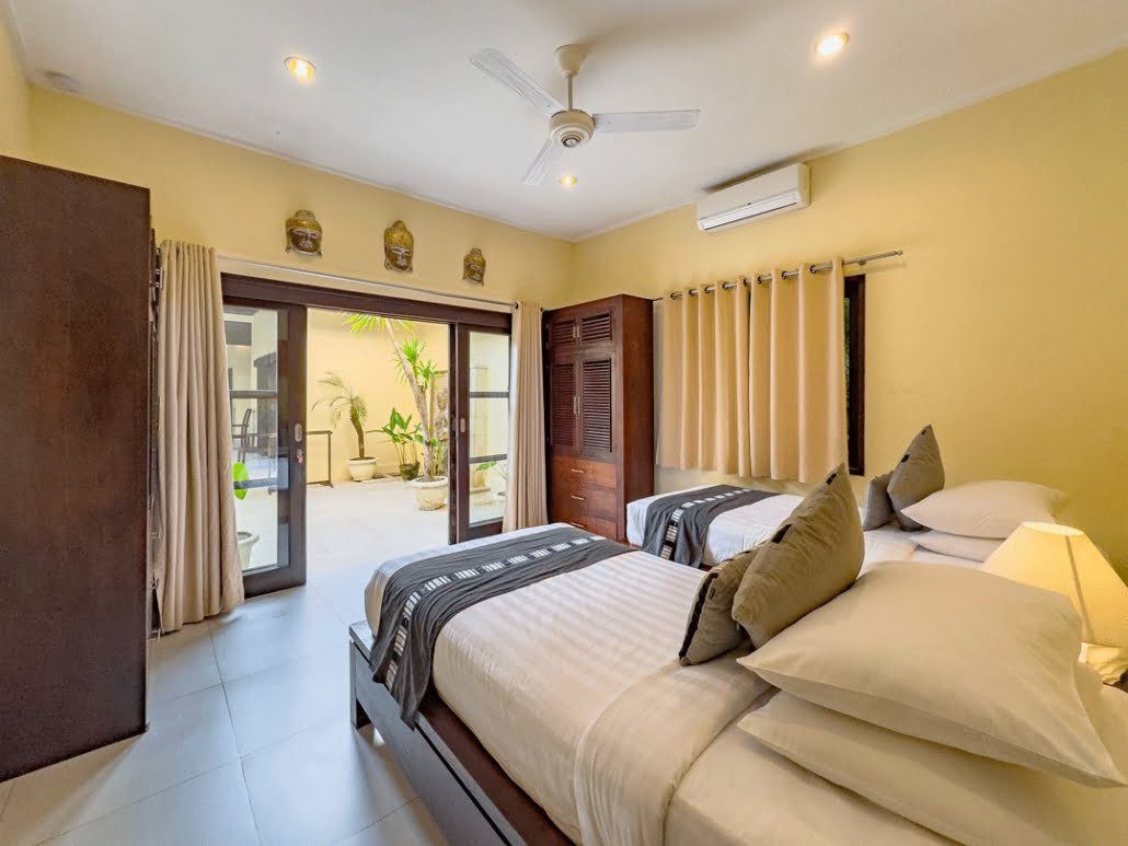 Airy twin bedroom 2 with pool views at Villa Tresna Seminyak by Villa Bugis Seminyak villas, equipped with air conditioning and comfortable double single beds.