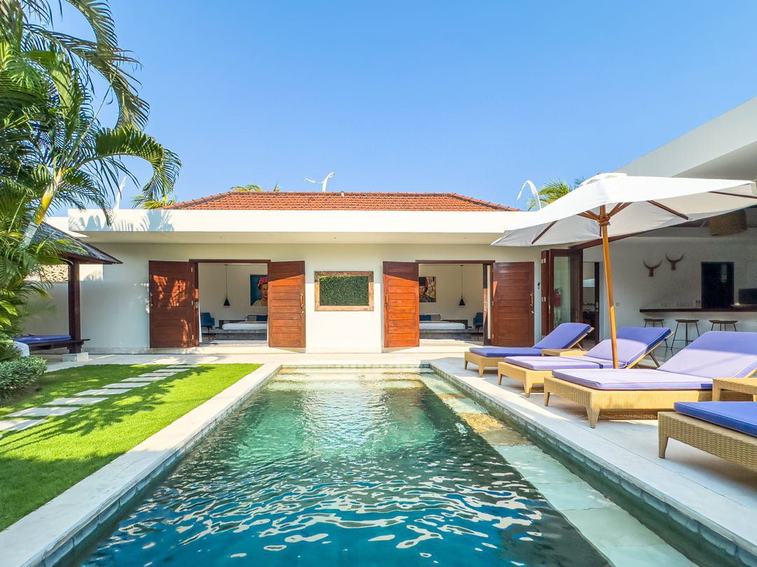 Sunlit private outdoor swimming pool surrounded by comfortable sun loungers and a lush tropical garden at Villa Umah Kupu-Kupu 2 Seminyak by Villa Bugis, a luxury villa Seminyak.