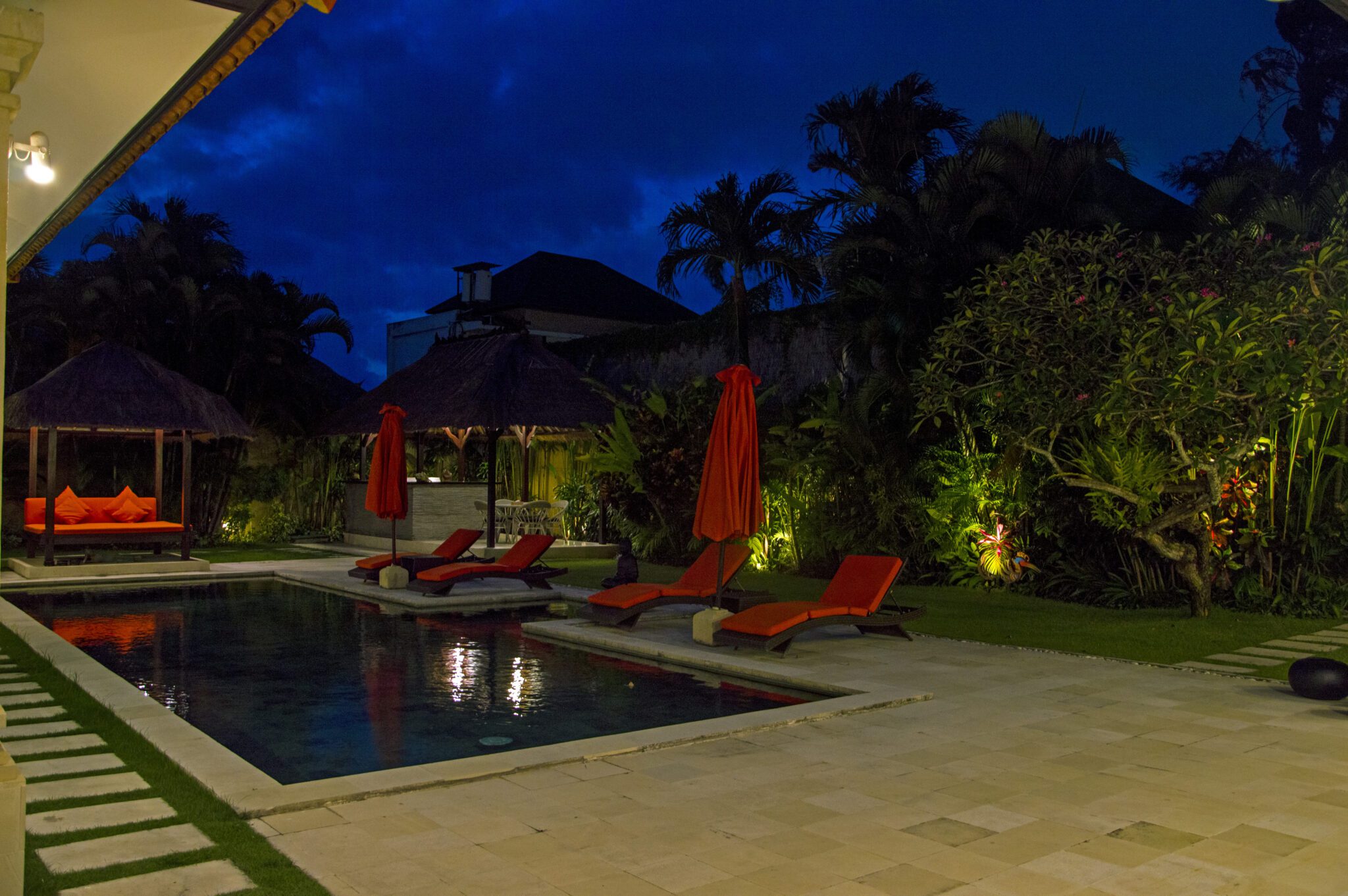 Cozy night view of the illuminated poolside patio and tropical garden at Villa Vara Seminyak by Villa Bugis villa Seminyak.