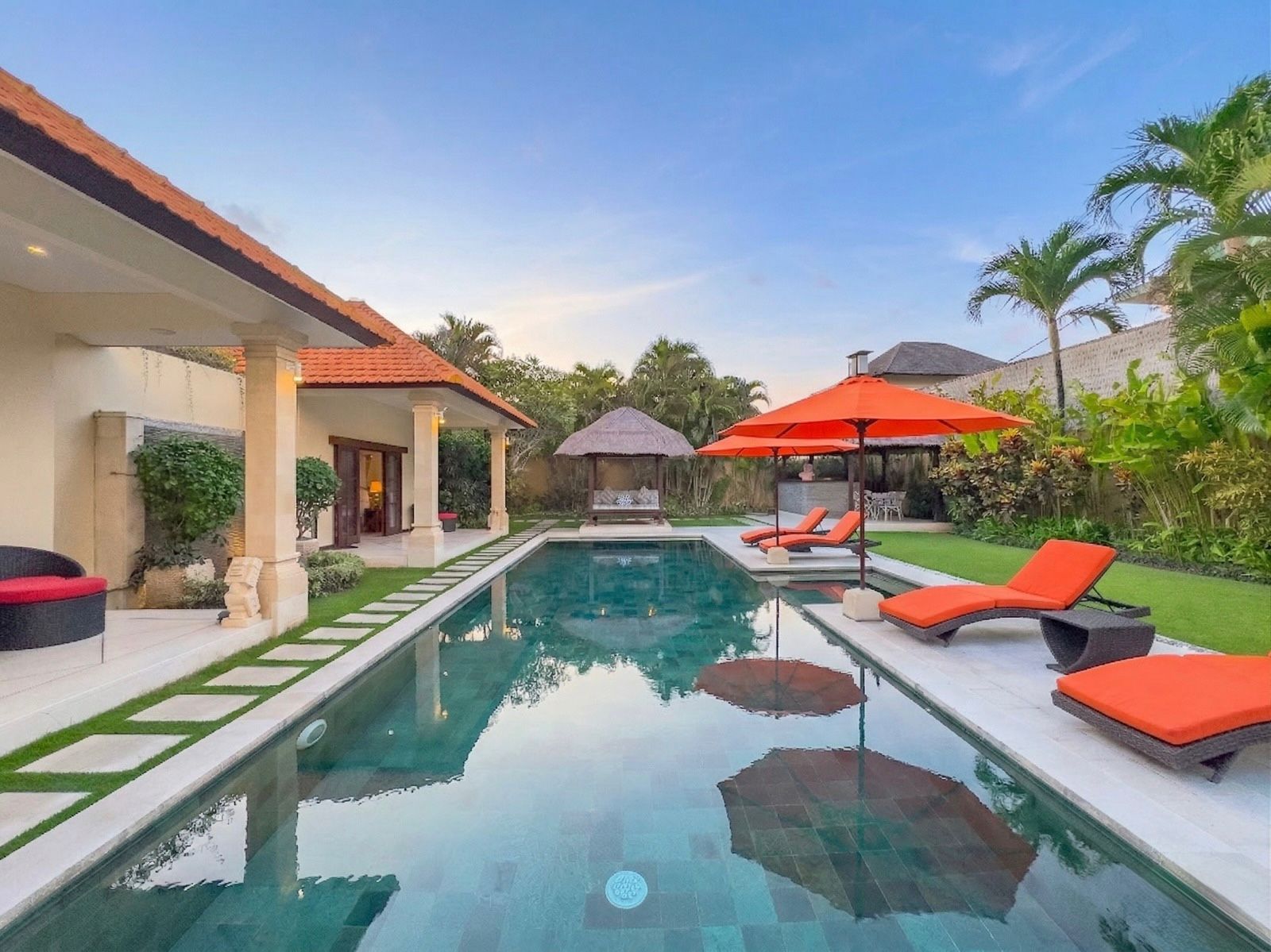 Sunlit private outdoor swimming pool surrounded by comfortable sun loungers and a lush tropical garden at Villa Vara Seminyak by Villa Bugis, a luxury villa Seminyak.